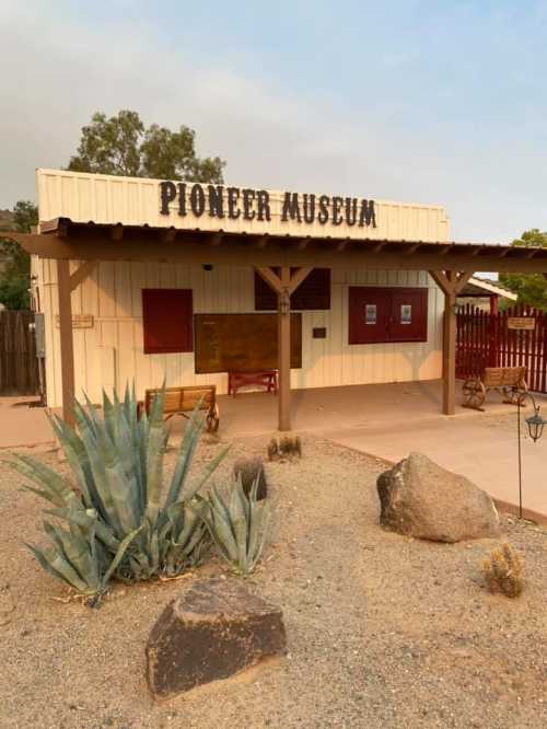 Exterior of the Pioneer Museum featuring a wooden building, desert landscaping, and a clear sky.