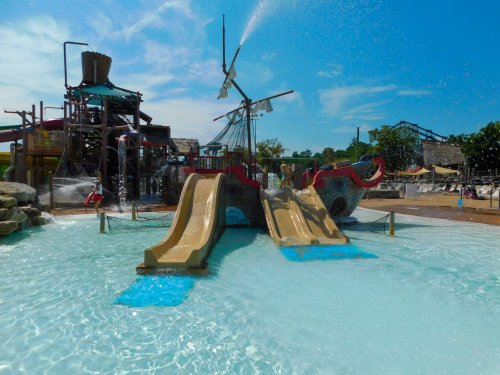 Water park featuring a pirate ship-themed play area with slides and splashing water under a clear blue sky.