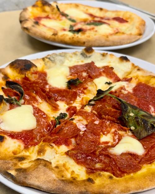 Two pizzas on plates: one topped with pepperoni and cheese, the other with cheese and basil.