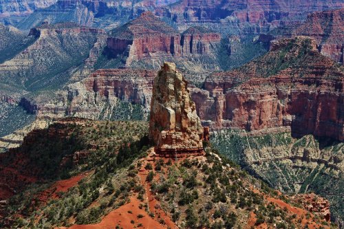 A rocky outcrop stands prominently in the foreground, surrounded by colorful canyon walls and rugged terrain.