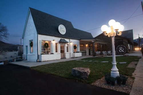 A charming white building with a sloped roof, decorated for the holidays, illuminated by a vintage streetlamp at dusk.