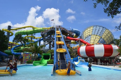 A vibrant water park featuring colorful slides, a large pool, and visitors enjoying the attractions under a sunny sky.