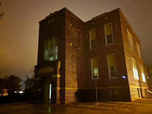A dimly lit brick building at night, with illuminated windows and a foggy atmosphere.