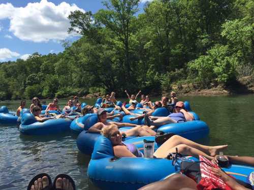 A group of people relaxing on blue inner tubes in a river, surrounded by trees and a sunny sky.