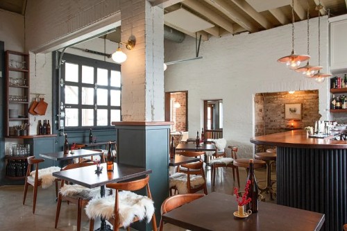 Cozy restaurant interior with wooden tables, chairs, and a bar, featuring warm lighting and rustic decor.