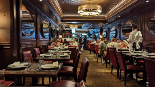 Elegant restaurant interior with wooden decor, round mirrors, and diners at tables, creating a warm atmosphere.