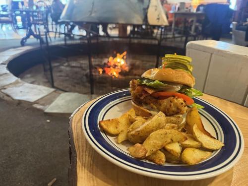A plate with a burger topped with lettuce, tomato, and pickles, served with golden potato wedges, near a cozy fire.