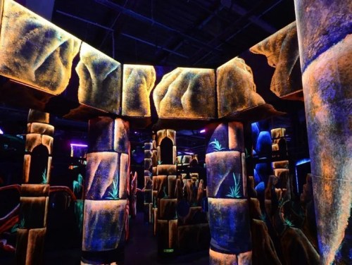 A vibrant, neon-lit indoor space with rock-like structures and colorful plants, resembling a cave or fantasy landscape.