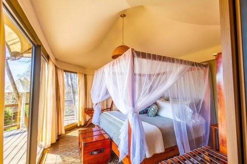 A cozy bedroom with a four-poster bed draped in white fabric, large windows, and wooden accents.