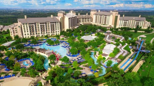 Aerial view of a large resort with pools, water slides, and lush landscaping under a blue sky.