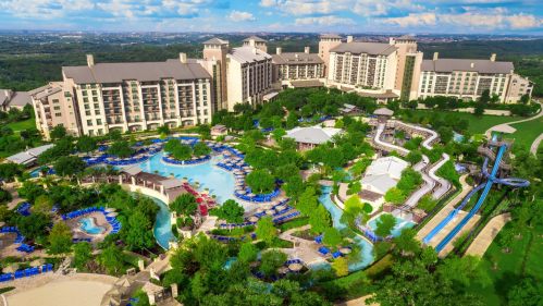 Aerial view of a large resort with pools, water slides, and lush landscaping under a blue sky.