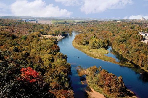 A scenic view of a winding river surrounded by colorful autumn foliage and rolling hills under a blue sky.