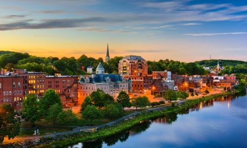 A scenic view of Augusta, the capital city of Maine, USA, featuring the State House dome surrounded by trees and set against a clear sky.