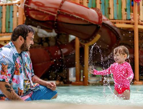 A man and a young girl play in a water park, splashing water and enjoying a fun day together.