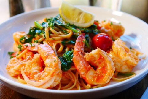 A plate of shrimp pasta topped with cherry tomatoes, greens, and a lemon wedge.