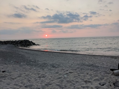 A serene beach scene at sunset, with gentle waves and a colorful sky reflecting on the water.