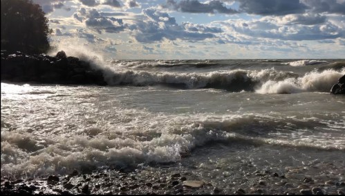 Waves crash against rocky shore under a cloudy sky, creating a dynamic seascape.
