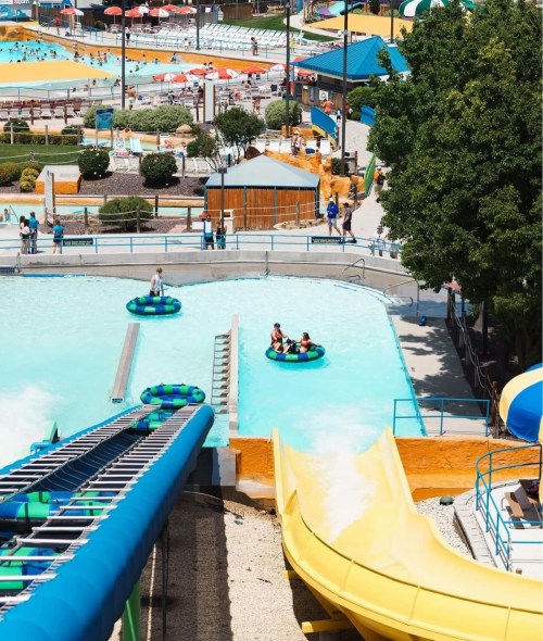 A vibrant water park scene featuring slides, a lazy river, and families enjoying the attractions under a sunny sky.