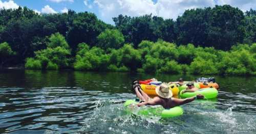 A group of people floating on colorful inner tubes in a river, surrounded by lush greenery and a blue sky.