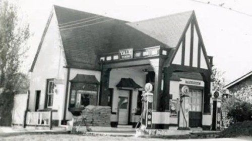 Historic black-and-white photo of a vintage gas station with a distinctive architectural style and old gas pumps.