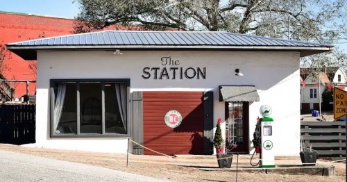 A small building with a sign reading "The Station," featuring a vintage gas pump outside and a rustic design.