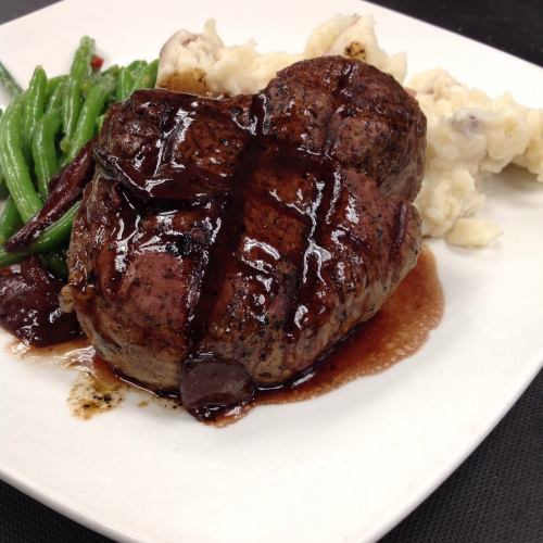 A perfectly cooked steak with grill marks, served with mashed potatoes and green beans on a white plate.