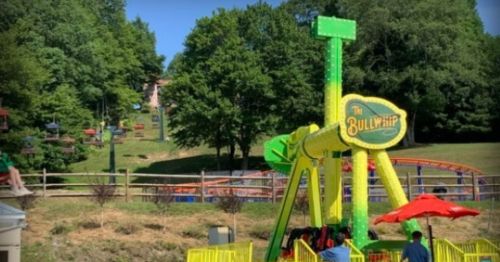 A colorful amusement ride called "The Bullywhip" in a park, with trees and a hillside in the background.