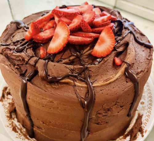 A chocolate cake topped with fresh strawberries and drizzled with chocolate sauce.