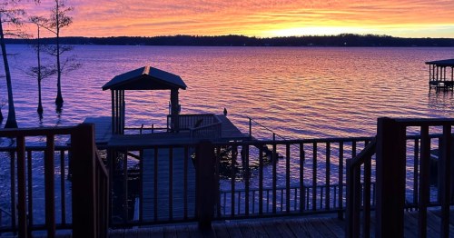 unset view of a Louisiana lakefront vacation rental with a private dock and scenic deck.