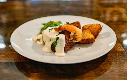 A plate featuring a beef filet topped with shrimp and creamy sauce, alongside green beans and roasted potatoes.