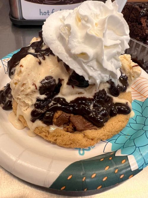A large dessert featuring a cookie base topped with ice cream, chocolate sauce, and whipped cream.