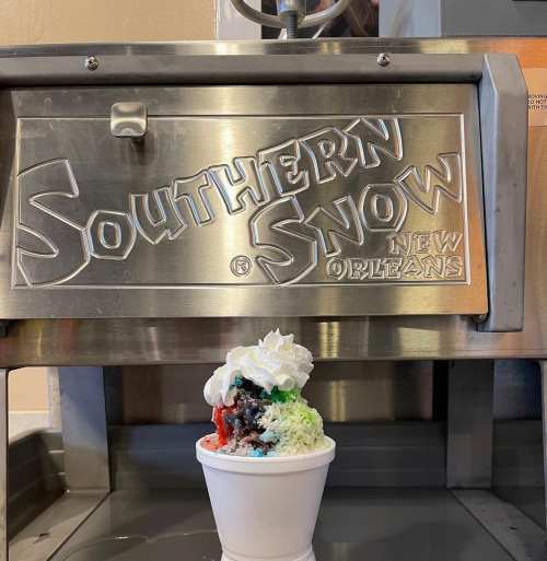 A cup of colorful snow cone topped with whipped cream in front of a Southern Snow machine.