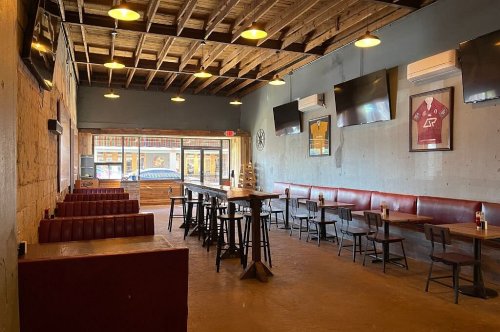 Interior of a casual restaurant with wooden tables, red booths, and multiple TVs on the walls. Bright and inviting atmosphere.