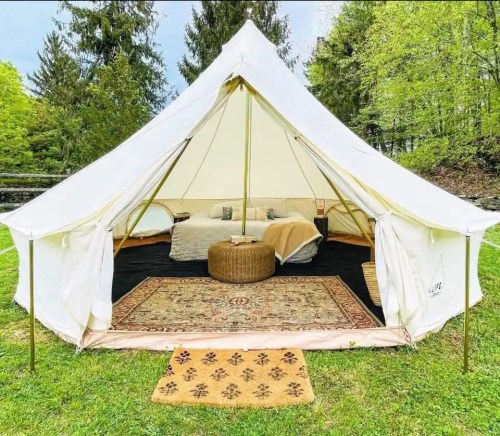 A spacious, cozy tent with a rug and cushions, set in a green outdoor area surrounded by trees.
