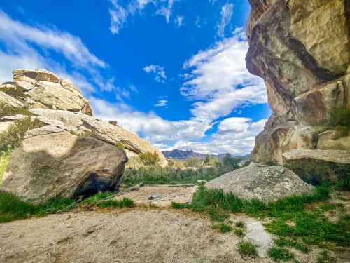 A scenic view of large boulders and grassy terrain under a bright blue sky with scattered clouds.