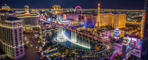 A vibrant night view of the Las Vegas Strip, featuring illuminated buildings and the Bellagio fountains.