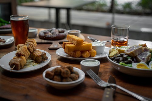 A table set with various dishes, including skewers, polenta, salad, and drinks, in a cozy dining setting.