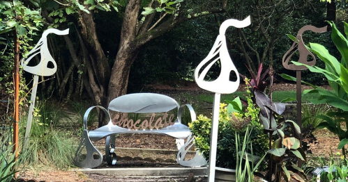 A whimsical garden scene featuring a metal bench with "chocolate" cutout and decorative chocolate-shaped sculptures.