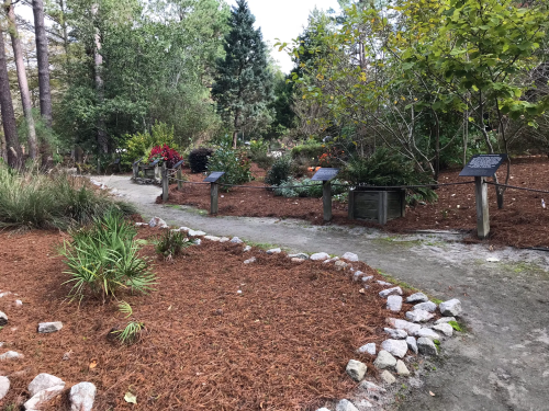 A winding garden path surrounded by lush greenery and flower beds, with informational signs along the way.