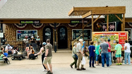A busy outdoor scene with people enjoying drinks and games outside a bar, surrounded by festive decorations.