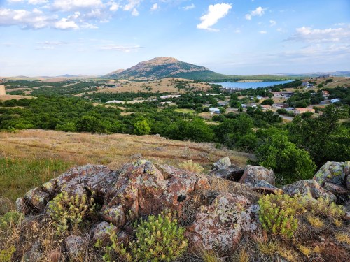 A scenic view of rolling hills and a distant mountain, with greenery and a small town visible in the valley below.