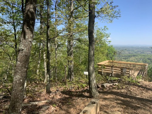 A scenic view from a wooded area, featuring trees and a wooden observation deck overlooking a valley.