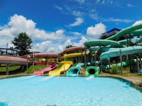 Colorful water slides twist and turn above a clear blue pool under a bright sky with fluffy clouds.
