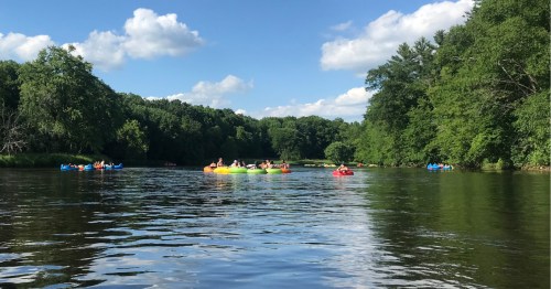 People tubing down a natural river with a bright, blue sky above.