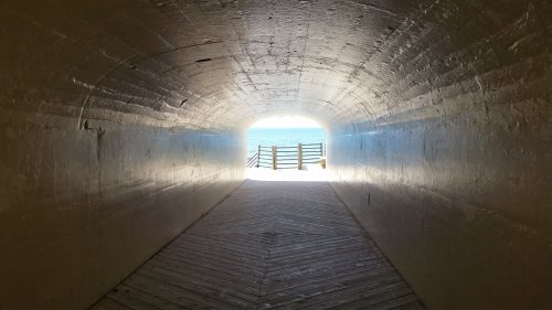 A tunnel leading to a bright exit, with wooden planks and a view of the ocean beyond.