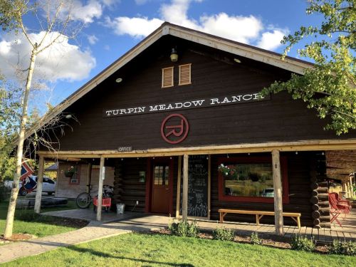 A rustic wooden building with a sign reading "Turpin Meadow Ranch," surrounded by greenery and blue skies.