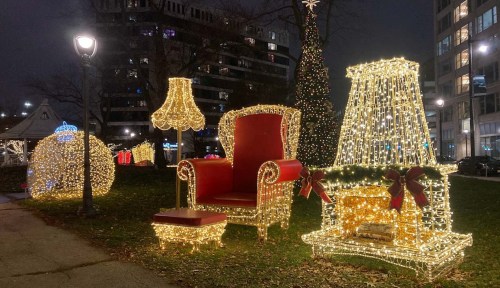 A festive display featuring a large red chair, a lamp, and a fireplace, all adorned with twinkling holiday lights.