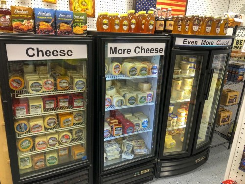 Three refrigerated displays filled with various types of cheese, labeled "Cheese," "More Cheese," and "Even More Cheese."