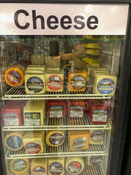 A refrigerated display case filled with various cheese blocks, labeled with different flavors and brands.