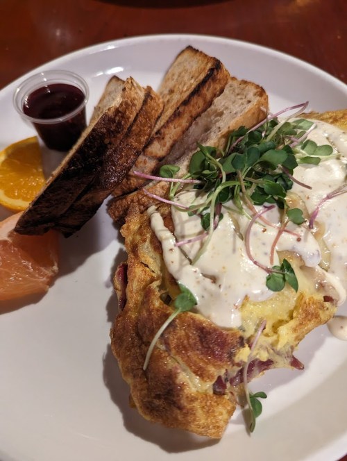 A plate featuring an omelet with sauce, toasted bread, and fresh fruit slices on the side.